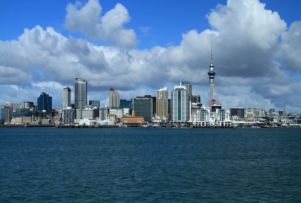 Vista de Auckland a partir da água, com a Sky Tower acima dos prédios e nuvens brancas.