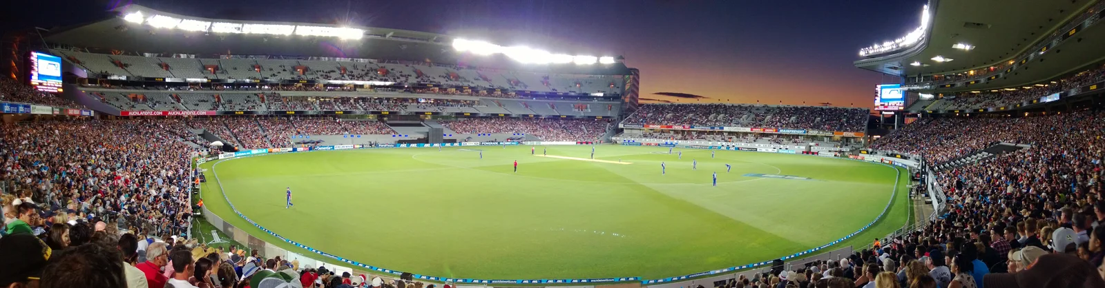 Vista panorâmica do Eden Park iluminado ao entardecer, durante uma partida de críquete em 2013.